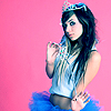 A person with long dark hair wears a blue tiara, light blue sleeveless top, and blue tutu against a solid pink background.