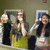 Four people stand in a against a wall with framed pictures; the rightmost person's face is blurred