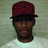 Pixelated static image of a person wearing a dark red cap with black brim and white shirt against muted green background.