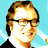 Pixelated static image of a person with light brown hair and glasses against a blue background, wearing dark clothing.