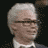 A 48x48 pixel animated contact sheet showing seven sequential frames of a man with white hair, glasses, and a dark suit against a black background, arranged in a 3x3 grid with one frame missing.