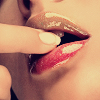 Close-up of a person's mouth with glossy red lips, a finger touching the lower lip, and visible teeth.