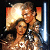 Pixelated static image of two figures in a close embrace with warm lighting and a blue light saber, set against dark background with orange rectangular shapes.