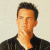 Static image of a person with short dark hair wearing a black jacket over a white shirt against a light background, next to green text reading 'Original Icons .com' on a dark green backdrop.