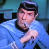 A person in a blue uniform with white stripes holds a thin white object near their mouth against a blurred background.