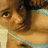 Pixelated close-up of a person with dark hair and light skin wearing a turquoise strap, set against warm brown tones.