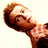 Pixelated static image of a person with brown hair and beard wearing a checkered shirt, viewed from an angle against a light background.