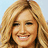 Pixelated close-up of a smiling person with long wavy blonde hair against light blue background.