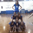 Pixelated image of a person in a blue outfit standing on a platform with a brown figure below, against a light background.