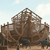 Pixelated static image of a brown wooden structure resembling a ship's hull with a lattice framework, set against a light blue sky with faint clouds.