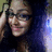 A pixelated close-up of a person with dark hair, wearing glasses, and a dark top against a gradient background.