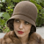 A pixelated portrait of a person wearing a light brown wide-brimmed hat, dark hair, and red lipstick, set against a green foliage background.