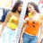 Two women in yellow and orange tops stand side-by-side, one holding a drink, against a blurred background.