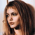 Pixelated close-up of a person with long brown hair, light skin, and dark eyes, facing left against a light background.