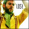 A person with green hair and beard wears a yellow jacket with brown straps and a green scarf, raising one arm against a bright background with the word 'LOST' in black text.