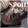 A hand with long nails and a large turquoise ring rests on a brown patterned clutch bag, overlaid with white text reading "SPOIL" and partial script.