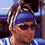 Pixelated static image of a person with dreadlocks wearing sunglasses and a blue headband, set against an indistinct background.