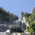 Pixelated landscape with rocky formations under a clear blue sky, green foliage on the right, and light-colored ground in the foreground.