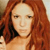 A pixelated close-up of a person with long, wavy reddish-brown hair, light skin, and neutral expression against a blurred background.