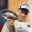 A pixelated image shows a person holding a large silver trophy against a blue background with text reading "Colts won XLI" and "and are gonna win it again".