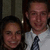 Two people in formal attire stand side-by-side against a dark background with vertical elements.