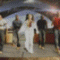 animated frames showing a woman in white clothing dancing with a group of men in dark and red outfits under a curved canopy