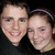 Two people in close proximity, one with a headband, against dark background.