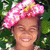 A person wearing a large pink bow with white polka dots on their head, set against a green leafy background.