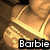 Pixelated image of a golden necklace with pendant on brown background, text 'Barbie' in white block letters at bottom.