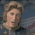 A four- animation of a figure with light brown hair wearing a blue garment with gold crosses, showing sequential facial expressions and hand movements against a blue background