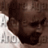 Pixelated static image of a person's face with brown skin tone, dark hair, and visible facial features including eyes, nose, mouth, and beard, set against a light background with partial white text on the left side.