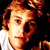 Pixelated static image of a person with light brown hair and fair skin wearing a white shirt against dark background.