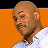 Pixelated image of a bald man with light brown skin wearing a white shirt against an orange background.