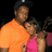 Pixelated image of two people standing close together against a dark background, one in an orange shirt and the other in a pink top.