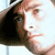 A pixelated close-up of a person's face with light skin tone, dark hair, and a dark-colored garment, set against a light background.