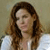 A pixelated image of a person with long brown hair wearing a white top against a muted background.