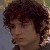 Pixelated close-up of a person with dark curly hair, light skin, and a neutral expression against a blurred background.