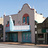 Pixelated image of a building with a light-colored facade, arched windows, and a blue sky background.