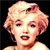Pixelated close-up of a person with light-colored curly hair, dark eyes, and red lips against a black background.