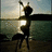 Pixelated figure in dark silhouette holding a light-colored object against a blurred background of water and sky.