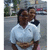 Two people in a light blue polo shirt and dark hair stand close together in an outdoor street scene with blurred background elements.