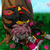 Pixelated static image of a character with brown hair and pink accents, standing in a green field under a light blue sky.