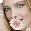 A woman with blonde hair and blue eyes holds a pink-and-white daisy in her mouth, smiling slightly while wearing light makeup.