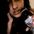 Pixelated image of a person with light brown hair wearing a black top, holding a phone to their ear and a small object in the other hand against a dark background.