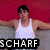 A person in a white tank top and dark cap sits with arms extended against a red background, with "SCHARF" text overlay.