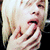 A person with light blonde hair covers their mouth with both hands in a gesture of surprise or shock, visible