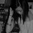 Black-and-white pixelated image of a person with long dark hair holding an object near their face, standing against a blurred background.