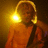 A pixelated figure in an orange outfit with a glowing yellow halo-like shape on the left side of its head, set against a dark brown background.