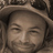 Static pixelated image of a person's face with closed eyes, wearing a dark head covering, against a blurred background.