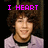 Two side-by-side pixelated images of a person with curly brown hair wearing a light purple jacket over a black shirt, each with distinct pink text above the head.